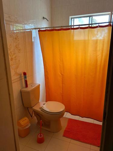 y baño con aseo y cortina de ducha de color naranja. en Casa Fransina, en Blue Bay