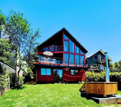 a large red house with a large deck on a yard at Espectacular casa Playa Hermosa, lagos y volcanes in Llanquihue
