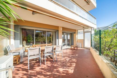 d'une terrasse avec des chaises blanches, une table et des fenêtres. dans l'établissement Nice one bedroom on the garden level, à Cannes