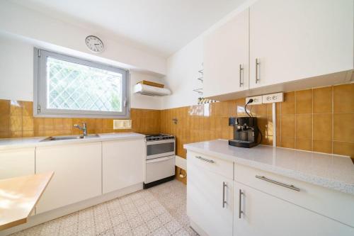 une cuisine avec des armoires blanches, un évier et une fenêtre dans l'établissement Nice one bedroom on the garden level, à Cannes