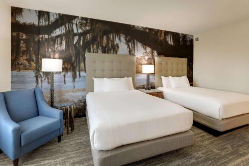 a bedroom with two beds and a blue chair at Drury Plaza Hotel Tallahassee in Tallahassee