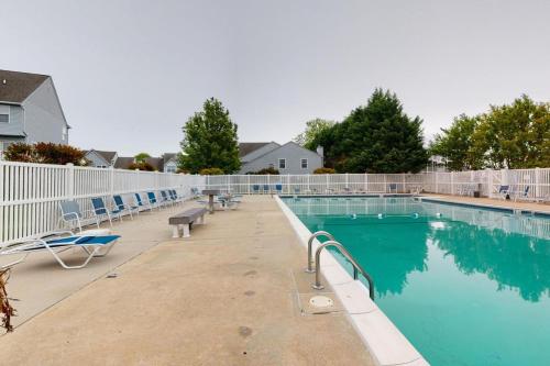 a swimming pool with chairs and a fence around it at Modern Beachside Bliss: 2 Bed/2 Bath Condo Haven in Rehoboth Beach