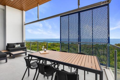 Absolute Beachfront 3 Bedroom Penthouse Bokarina Sunshine Coast في كاوانا ووترز: شرفة مع طاولة وكراسي خشبية والمحيط
