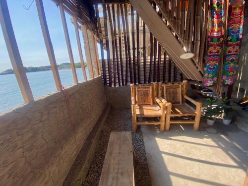 a balcony with two chairs and a view of the water at Kubo house by the water in ELYU, Ba-ey Ad Shanom in San Fernando