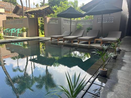 a pool with chairs and umbrellas in a yard at BK Beach Boutique Hotel - Hikkaduwa in Hikkaduwa