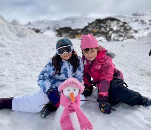 two young girls sitting in the snow with a snowman at Smiggins Hotel & Chalet Apartments in Perisher Valley