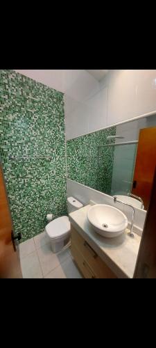 a bathroom with a sink and a toilet and green tiles at Condominio Dumont in Canoas