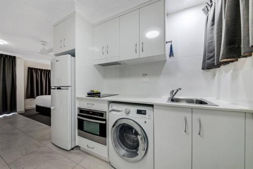 eine weiße Küche mit einer Waschmaschine und einem Waschbecken in der Unterkunft Deluxe King Studio + top floor sea views in Emu Park