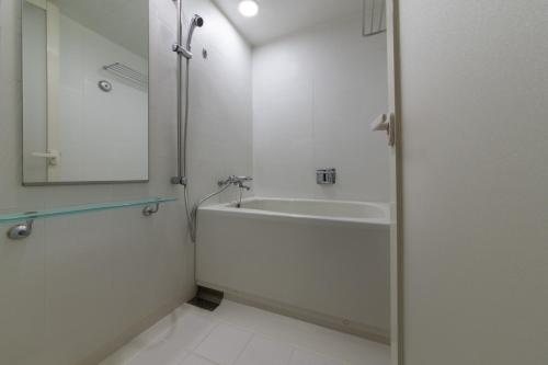 a bathroom with a tub and a sink and a mirror at Hotel Vista Kumamoto Airport in Ozu