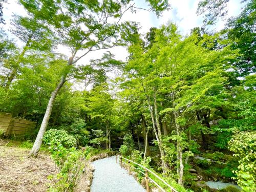 a path through a forest with trees and a bridge at Hakone Kowakien Hotel in Hakone
