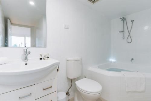 a white bathroom with a toilet and a sink and a tub at Lakeside 3-Bed Apartment with Jacuzzi in Belconnen