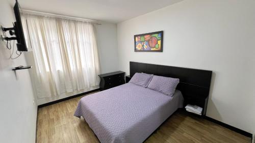 een slaapkamer met een bed met paarse lakens en een raam bij Hermoso loft a una cuadra del parque principal in Líbano