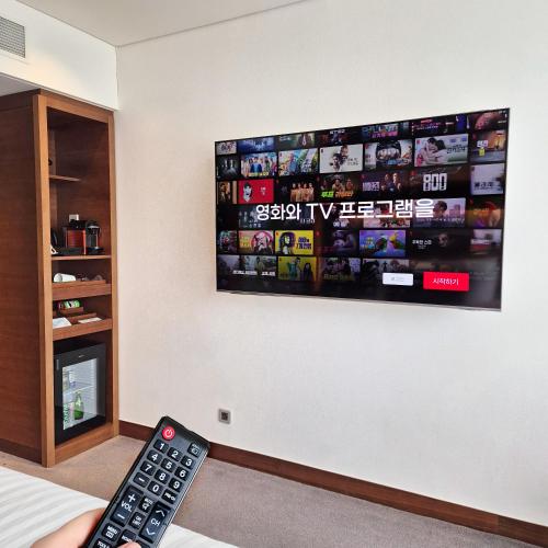 a remote control laying on a bed with a tv on a wall at Novotel Ambassador Suwon in Suwon