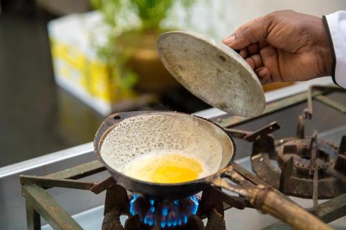 une personne cuisine un œuf dans un pot sur une cuisinière dans l'établissement Kudaoya Bungalow, à Rattota