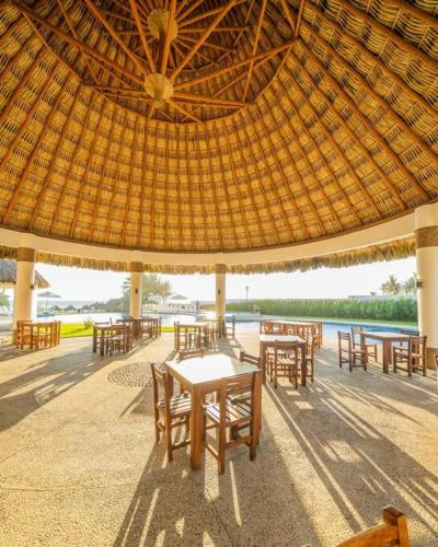 a patio with tables and chairs under a straw umbrella at Departamento Boutique con más Amenidades que Ningún otro en la Zona in Acapulco