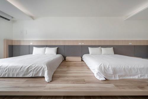 two beds in a room with white sheets and wood floors at Taitung Spring Homestay B&B in Taitung City