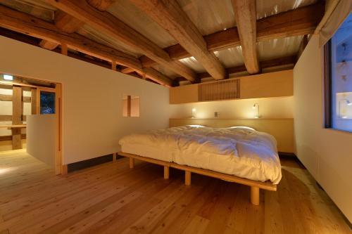 a bed in a room with a wooden ceiling at 一棟貸し古民家の宿まるがやつ in Ōtaki