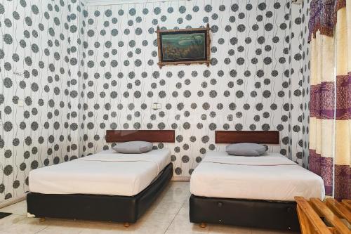two twin beds in a room with a wall at Hotel Jaya Wisata RedPartner in Sungaipenuh