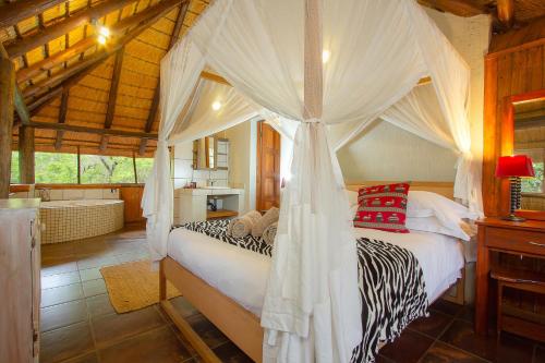 a bedroom with a canopy bed and a bathroom at Marloth Kruger Little Manor in Marloth Park