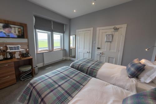 a bedroom with two beds and a desk and window at Northern Sands Hotel in Dunnet