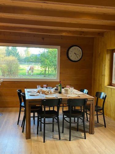 une salle à manger avec une table, des chaises et une horloge dans l'établissement Chalet en bordure de forêt, à Betton