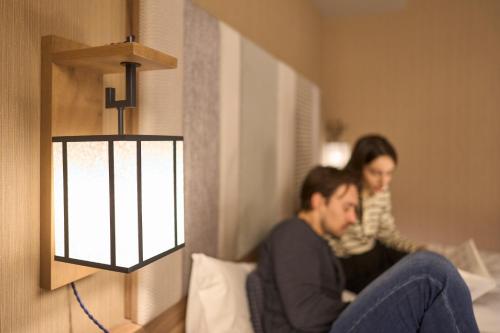 a man sitting on a bed next to a woman at Hotel Resol Kyoto Shijo Muromachi in Kyoto