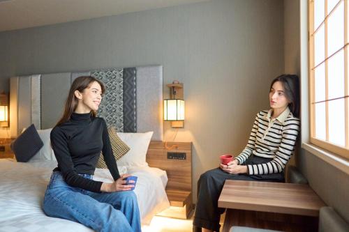 two women sitting on beds in a hotel room at Hotel Resol Kyoto Shijo Muromachi in Kyoto