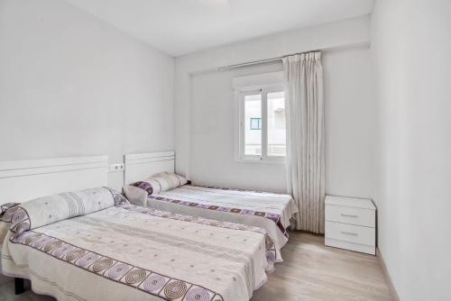 3 camas en una habitación blanca con ventana en Cala Blanca, en Playa de Gandía