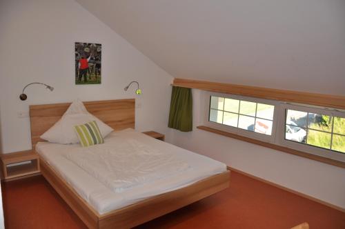 ein kleines Schlafzimmer mit einem Bett und zwei Fenstern in der Unterkunft Gästehaus Eisenhut in Walzenhausen