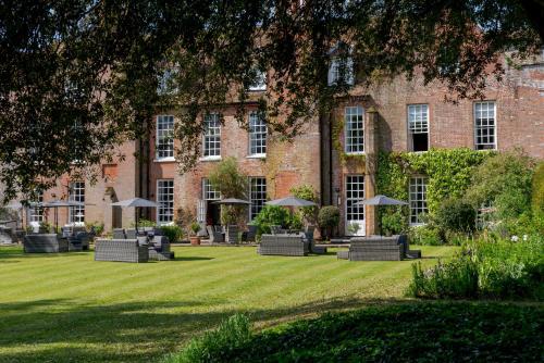 a building with chairs and umbrellas in the grass at Hintlesham Hall Hotel in Ipswich