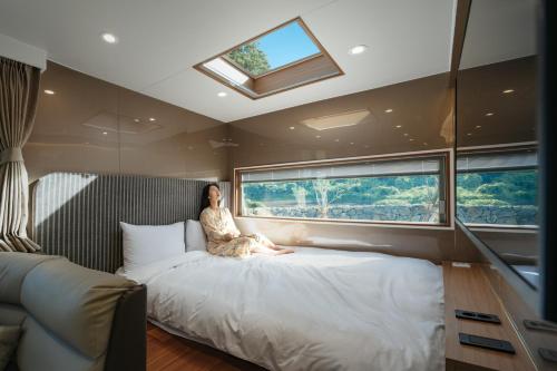 uma mulher sentada numa cama num quarto com uma janela em Yakmaeul em Seogwipo