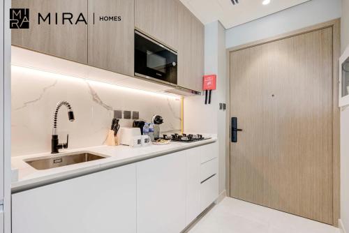 a white kitchen with a sink and a door at Mira Holiday Homes-Cozy studio close to metro in Dubai