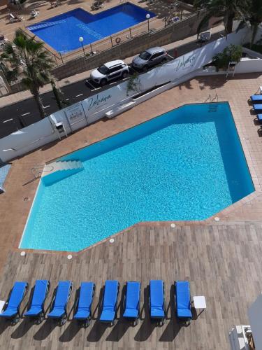 uma vista superior de duas piscinas com cadeiras azuis em Studio Ponderosa em Playa de las Americas