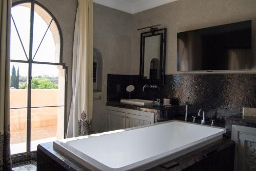 La salle de bains est pourvue d'une grande baignoire blanche et d'une fenêtre. dans l'établissement Palais Laawina, à Marrakech