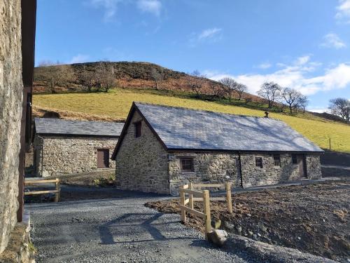 an old stone barn with a hill in the background at Cwm Clyd Longhouse in Llanwrthwl