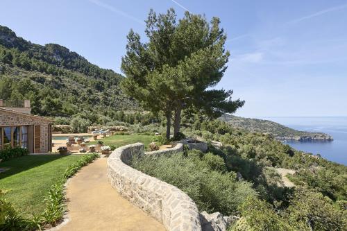 Villa Can Miquelet Deia في دِيّا: جدار حجري محتفظ به أمام منزل به شجرة