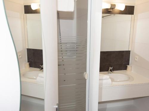 a bathroom with two sinks and two mirrors at Cit'Hotel Les Eleis in Saint-Martin-de-Fraigneau