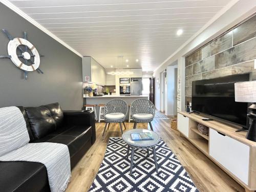 ein Wohnzimmer mit einem schwarzen Ledersofa und einem TV in der Unterkunft Coastal Hospitality - De Valle 65 in Mossel Bay