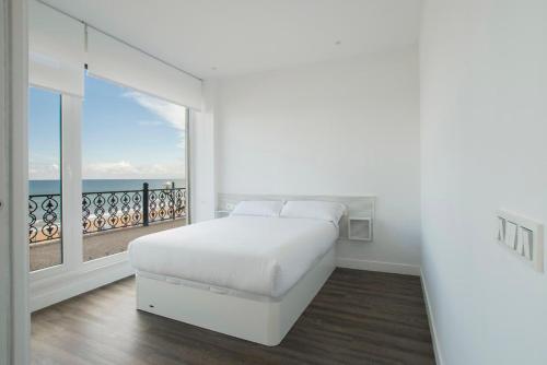 a white bedroom with a bed and a large window at Egona - Good Duke in Zarautz