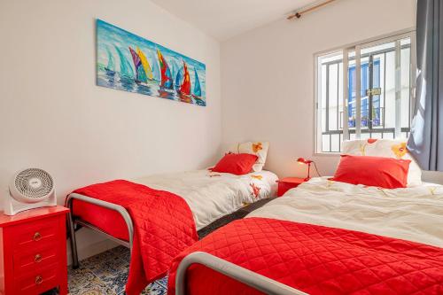 a bedroom with two beds with red sheets and a window at Casa Marlo, Spacious House in the Lively Centre of Cómpeta in Cómpeta