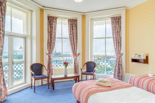 a hotel room with two beds and two chairs and windows at Queens Hotel in Eastbourne