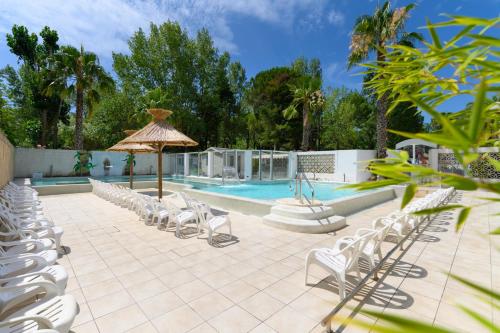 uma piscina com cadeiras brancas e um guarda-sol e uma piscina em Camping L'EDEN em Le Grau-du-Roi
