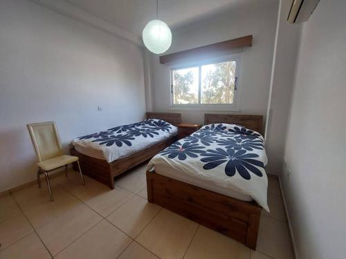two beds in a room with a window and a chair at Sunny 2 Bedroom Larnaca Center in Larnaka