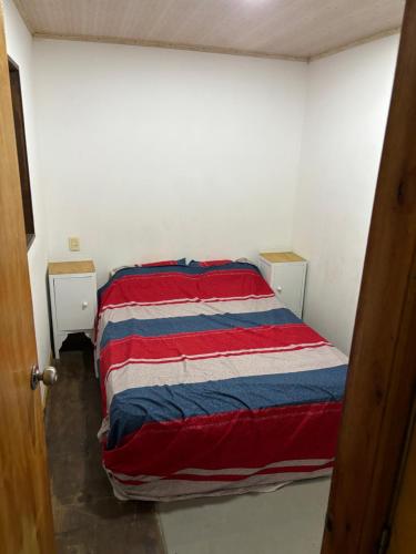 Cama en habitación con manta roja blanca y azul en Casa roja, en Fray Bentos