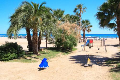 uma praia arenosa com palmeiras e um parque infantil em Beach Apartment Regueral em Cambrils