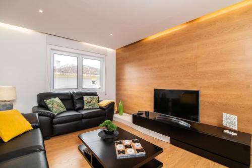 a living room with a black leather couch and a flat screen tv at Alojamento Encantador no Centro de Ponta Delgada in Ponta Delgada