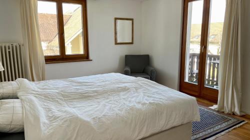 a bedroom with a white bed and a chair and windows at Gemütliches Haus mit Seeblick in Ermatingen