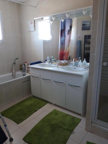 La salle de bains est pourvue de 2 lavabos, d'un miroir et de tapis verts. dans l'établissement Maison confort entre Bassin et Ocean, à Lège-Cap-Ferret
