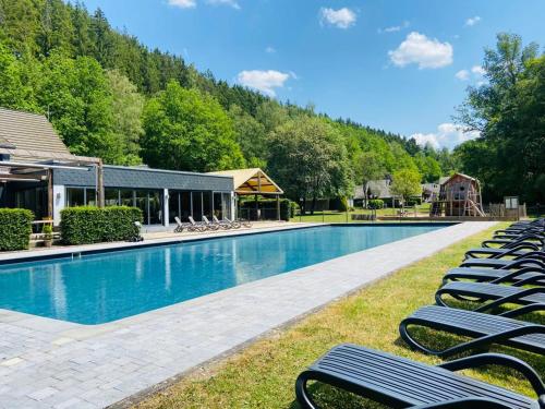 a large swimming pool with lounge chairs in front of a house at Hotel Le Val D'arimont in Malmedy
