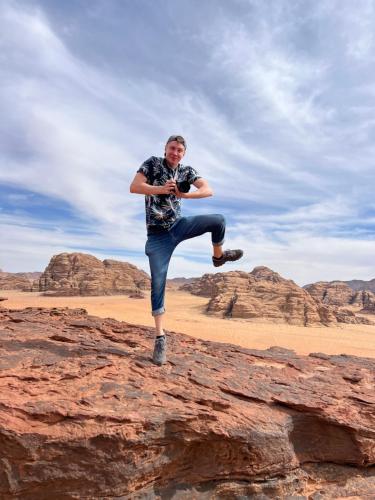 a man jumping on a rock in the desert at desert colored camp in Wadi Rum